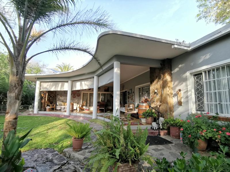 A spacious covered patio featuring a distinctive curved roofline, stone feature wall, and direct access to the landscaped garden area.