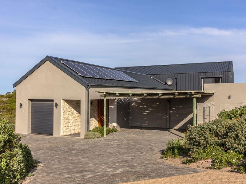 Modern architectural home featuring stone cladding, metal roofing with solar panels, a paved driveway, and a timber pergola entrance.