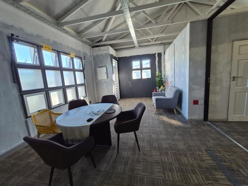 An office space featuring exposed steel roof trusses, carpeted flooring, and unfinished wall surfaces, offering a blank canvas for custom interior design.