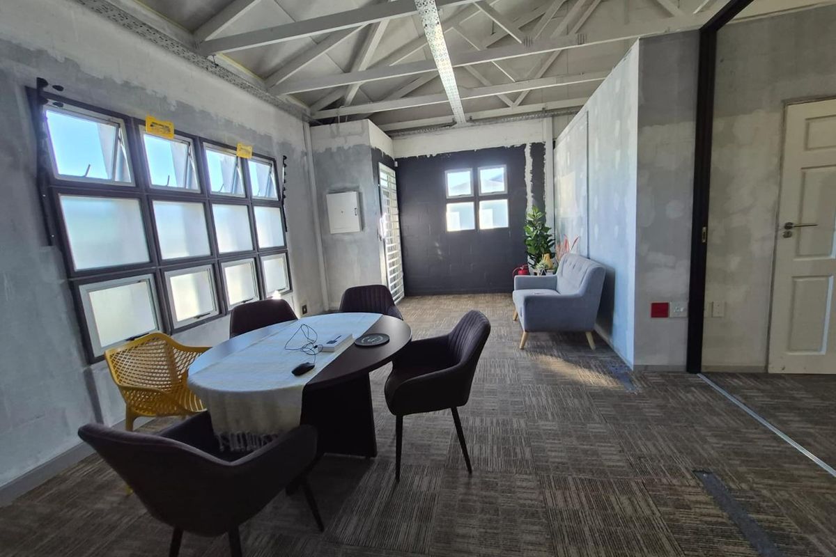 An office space featuring exposed steel roof trusses, carpeted flooring, and unfinished wall surfaces, offering a blank canvas for custom interior design.