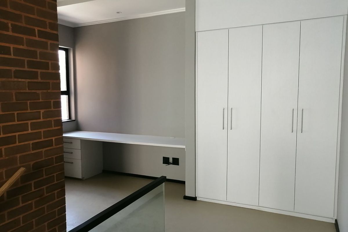 A modern bedroom featuring built-in white cabinetry, a sleek integrated desk workspace, and a striking exposed brick feature wall.