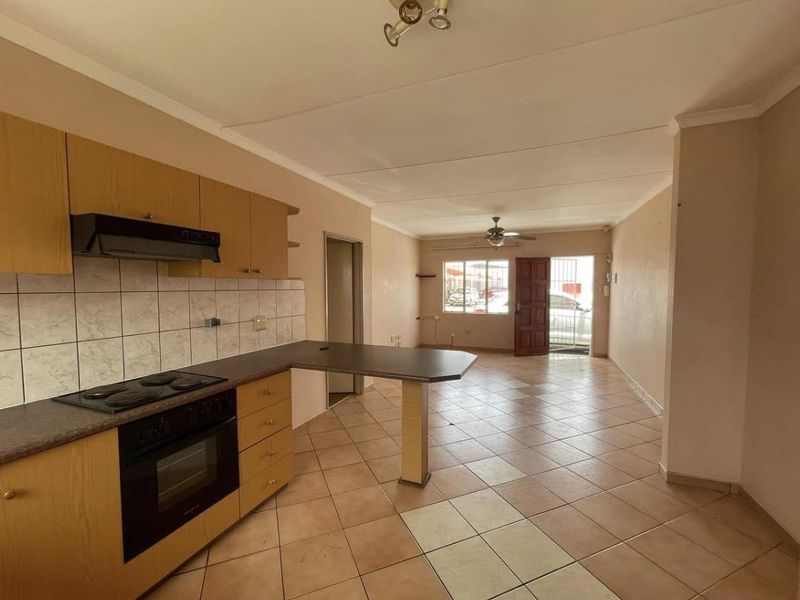 Open-plan kitchen and living area featuring tiled flooring, built-in cabinetry with integrated appliances, and direct access to the exterior via a security gate.