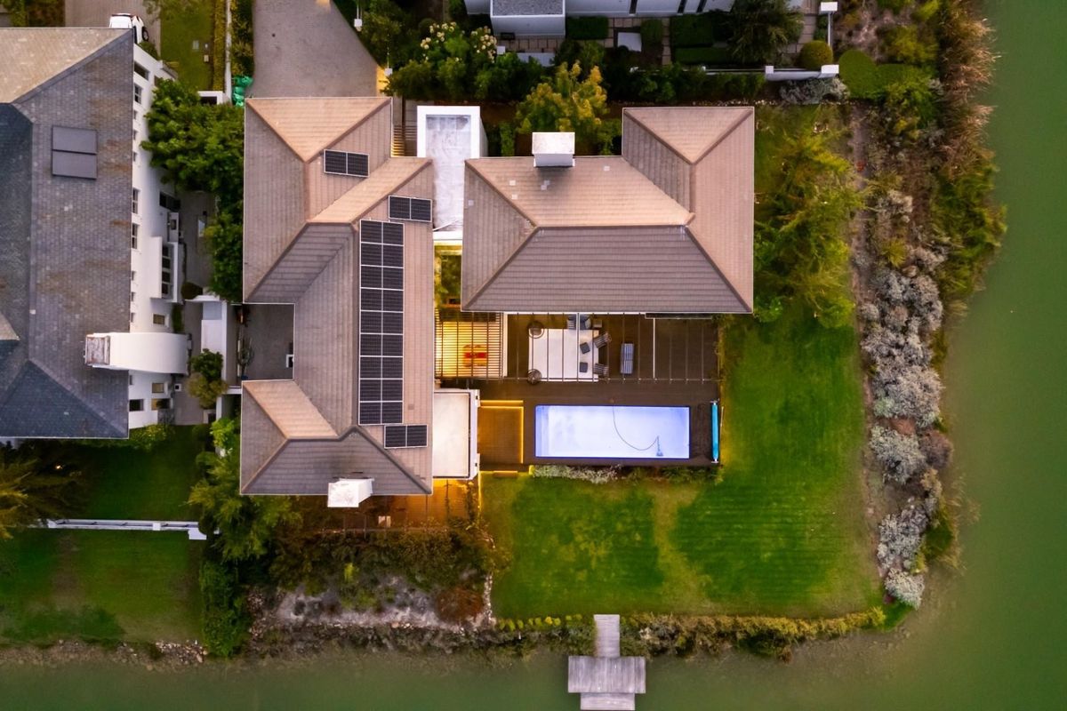 Aerial view of a waterfront property featuring a tiled roof, solar panels, a swimming pool, and a private jetty on the water's edge.