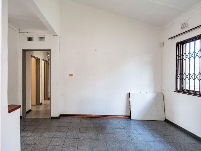 An empty living area featuring tiled flooring, security bars on the window, and neutral walls, offering a blank canvas for renovation.