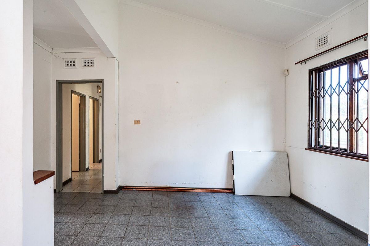 An empty living area featuring tiled flooring, security bars on the window, and neutral walls, offering a blank canvas for renovation.