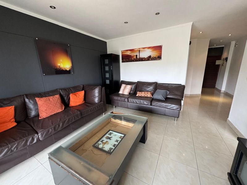 A well-lit living room featuring neutral tiled flooring, recessed ceiling downlights, and a modern dark accent wall.