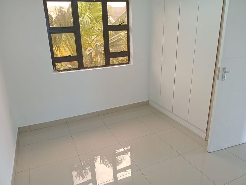 A clean, empty bedroom featuring neutral tiled flooring, built-in cupboards, and an aluminium-framed window providing natural light.