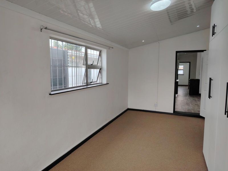 A clean, empty bedroom featuring neutral carpeting, built-in cupboards, and a window with security bars, offering a bright and versatile living space.