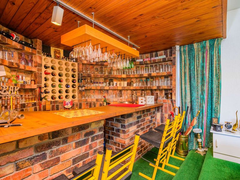 A rustic home bar area featuring exposed brick walls, a timber-clad ceiling, built-in wine storage, and a dedicated glassware hanging rack.
