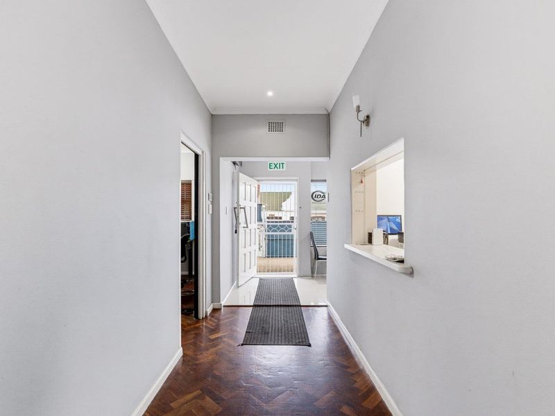 A bright, clean hallway featuring classic herringbone timber flooring, a service window opening, and a secure entrance door leading to the exterior.