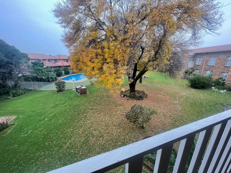 Elevated view overlooking a well-maintained communal garden, mature trees, and a swimming pool area within the apartment complex.