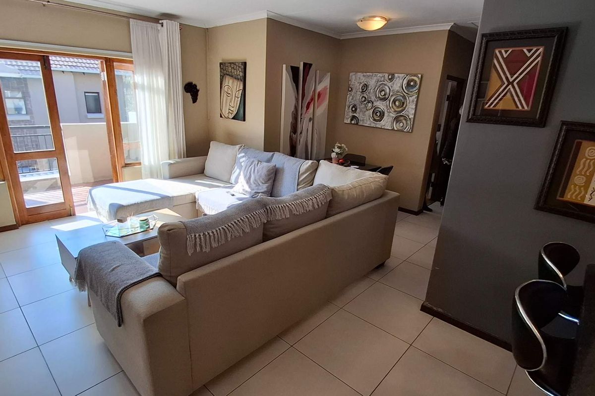 A well-maintained living room featuring neutral tiled flooring and a large sliding glass door providing access to an outdoor balcony area.
