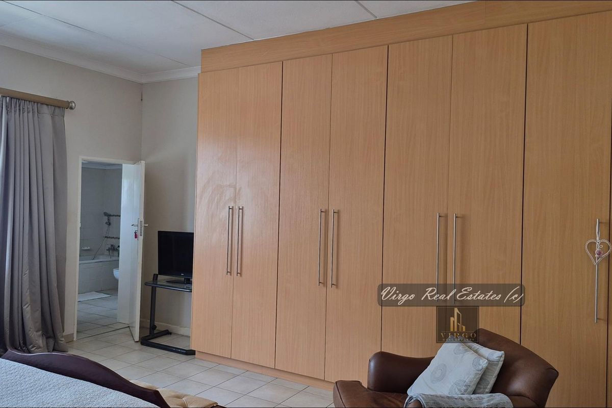 Spacious bedroom featuring extensive built-in wooden cupboards, tiled flooring, and direct access to an en-suite bathroom.