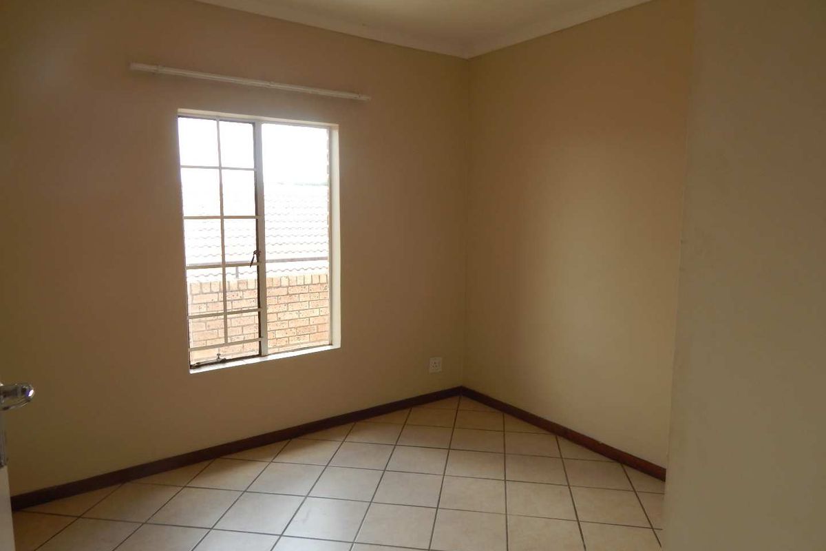 An empty bedroom featuring neutral wall paint, tiled flooring, and a window with security bars.