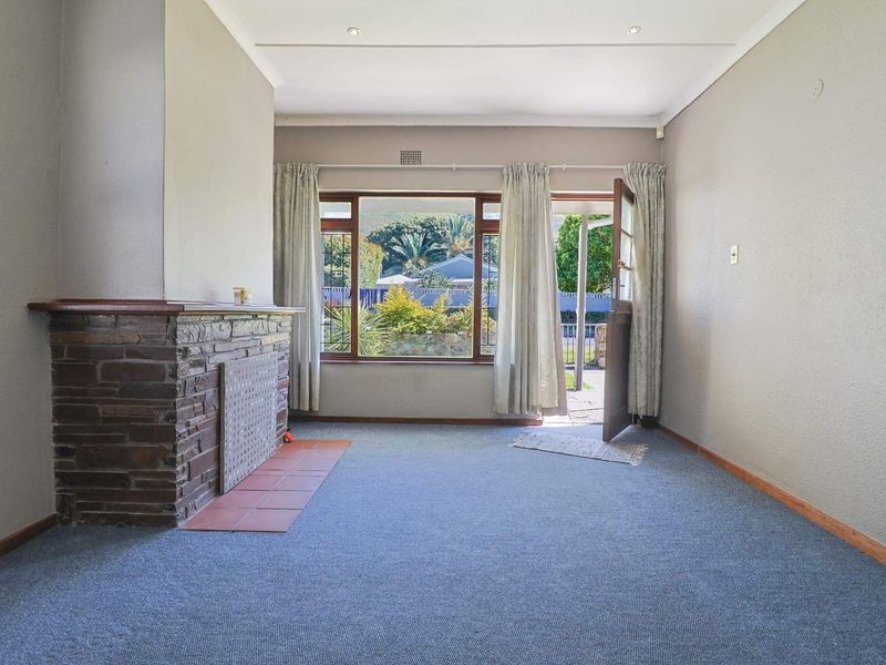 An empty living room featuring a stone fireplace with a tiled hearth, recessed lighting, and direct access to the garden through a timber door.