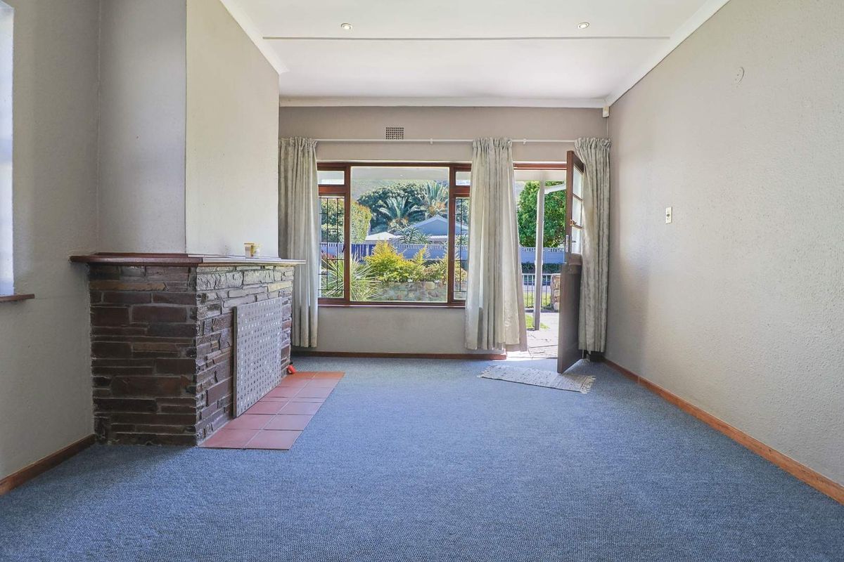 An empty living room featuring a stone fireplace with a tiled hearth, recessed lighting, and direct access to the garden through a timber door.