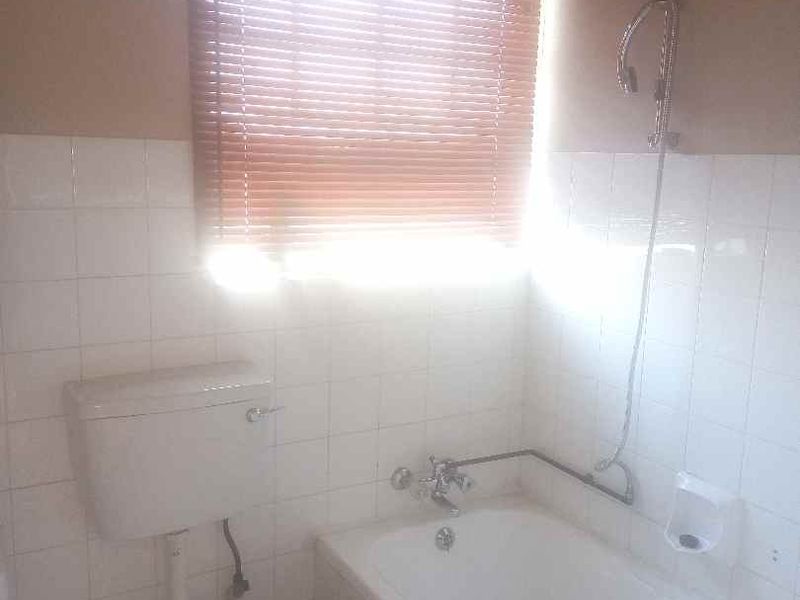 A functional bathroom featuring a standard bathtub with shower attachment, toilet, and tiled walls, illuminated by natural light through a window with blinds.