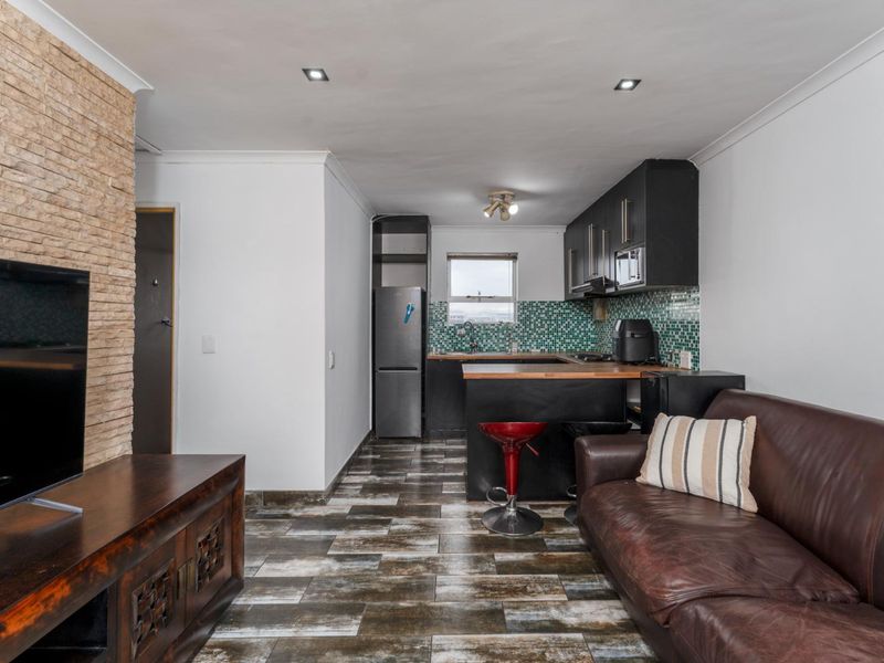 Open-plan living area featuring a stone-clad feature wall, tiled flooring, and a compact kitchen with mosaic backsplash and dark cabinetry.