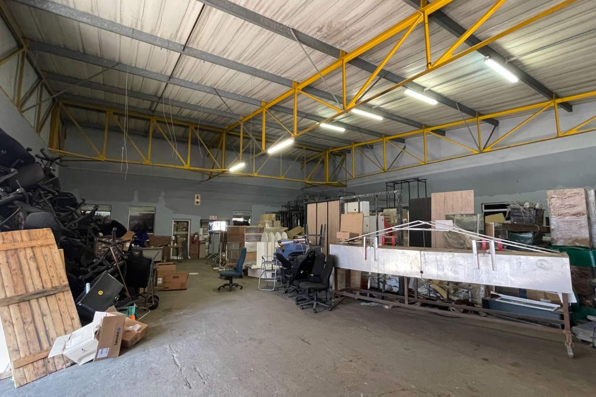 Spacious industrial utility area featuring exposed yellow steel roof trusses, concrete flooring, and fluorescent lighting, suitable for storage or workshop use.