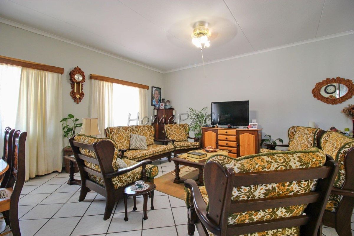 A spacious living room featuring tiled flooring, a ceiling fan, and large windows that provide natural light.