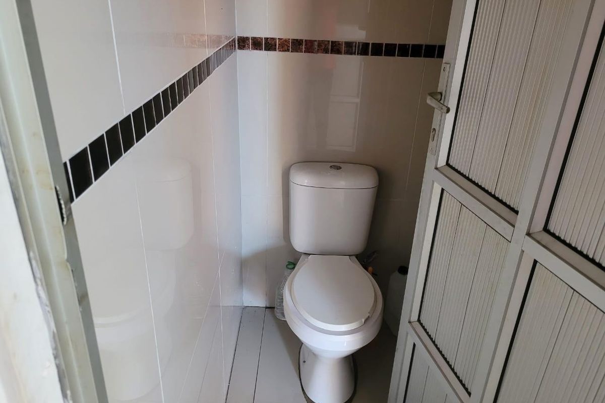 A compact bathroom featuring white ceramic wall and floor tiles with a decorative accent border and a standard white toilet.