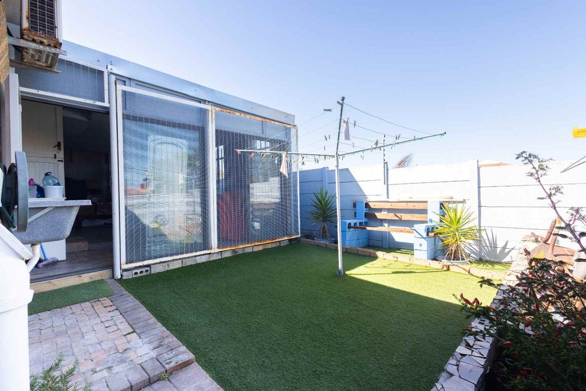 A compact rear garden area featuring artificial turf, a paved walkway, a washing line, and a partially enclosed patio structure.