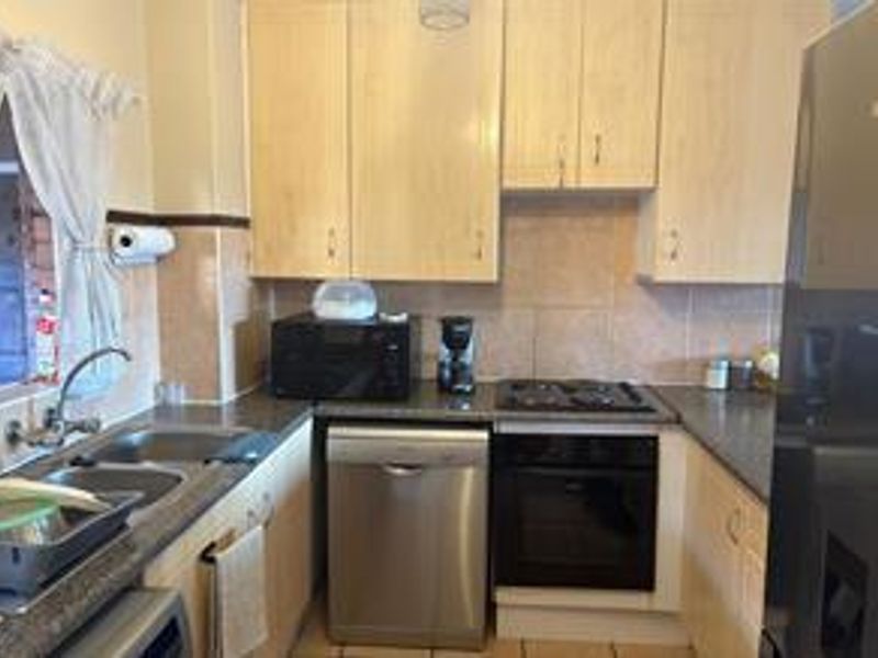 A functional kitchen featuring light wood-finish cabinetry, tiled backsplash, built-in oven, hob, and a double basin sink with a mixer tap.