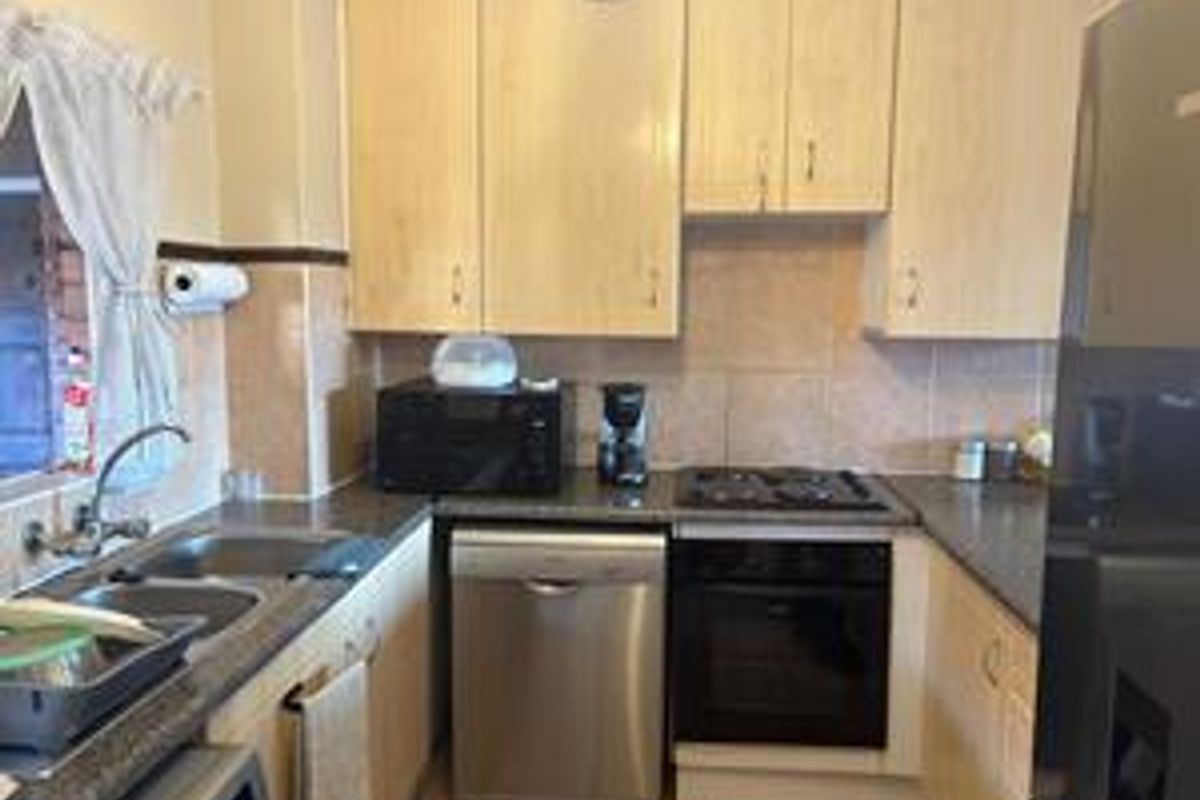 A functional kitchen featuring light wood-finish cabinetry, tiled backsplash, built-in oven, hob, and a double basin sink with a mixer tap.