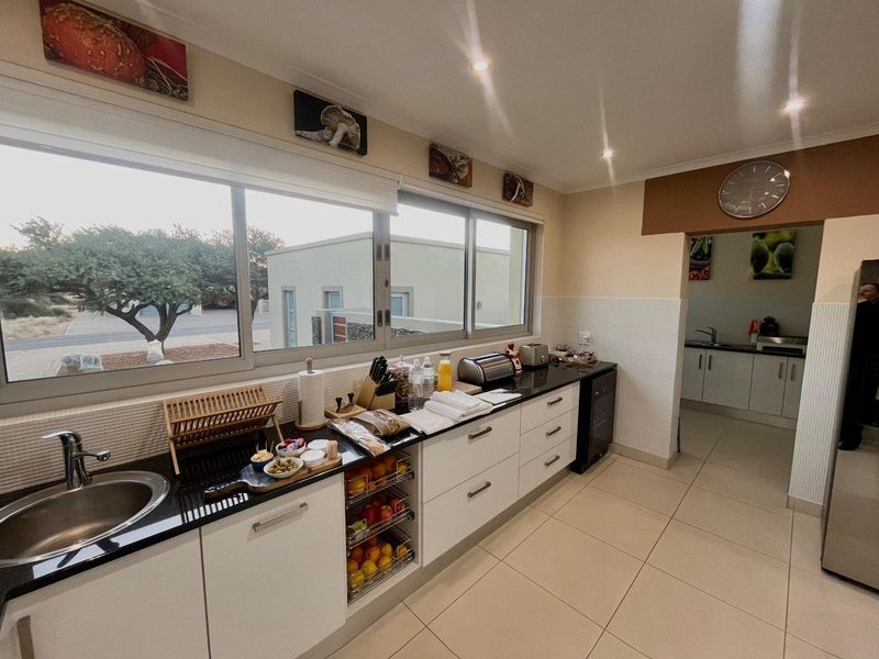A functional kitchen featuring white cabinetry, black granite countertops, mosaic tile backsplash, and large sliding windows providing natural light.