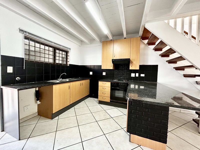 A functional kitchen featuring granite countertops, built-in oven, extractor fan, and tiled flooring, situated beneath an open staircase with exposed ceiling beams.