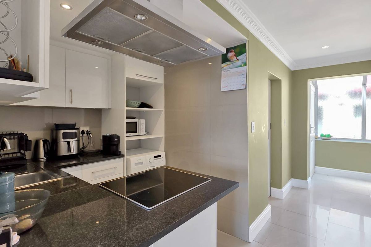 Modern kitchen featuring granite countertops, a built-in electric hob, stainless steel extractor fan, and sleek white cabinetry with recessed lighting and tiled floors.