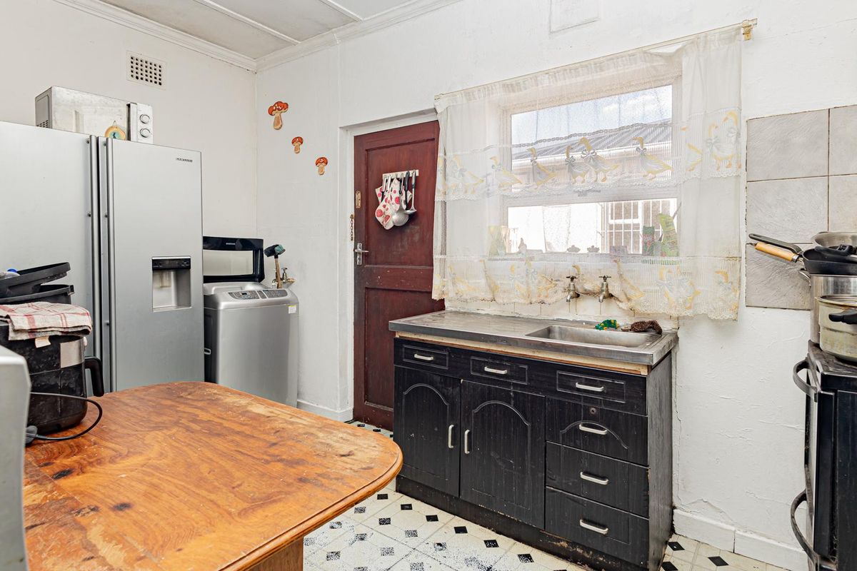 A dated kitchen featuring original cabinetry, a stainless steel sink, and tiled flooring, offering significant potential for modernization and renovation.