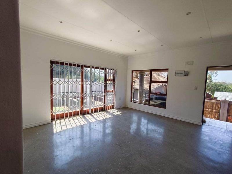 Spacious, empty living area featuring polished concrete floors, recessed lighting, and large sliding doors with security gates leading to the exterior.