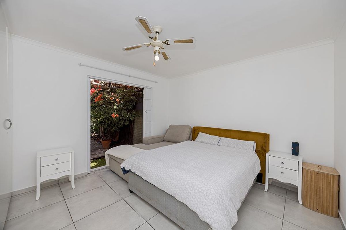 A bright bedroom featuring tiled flooring, a ceiling fan, and a sliding glass door providing direct access to the garden area.