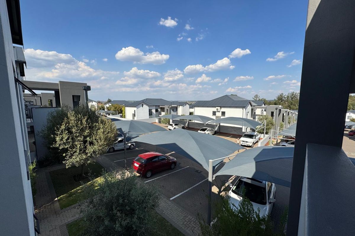 An elevated view of the apartment complex parking area featuring paved driveways, landscaped garden sections, and modern shade cloth carports.