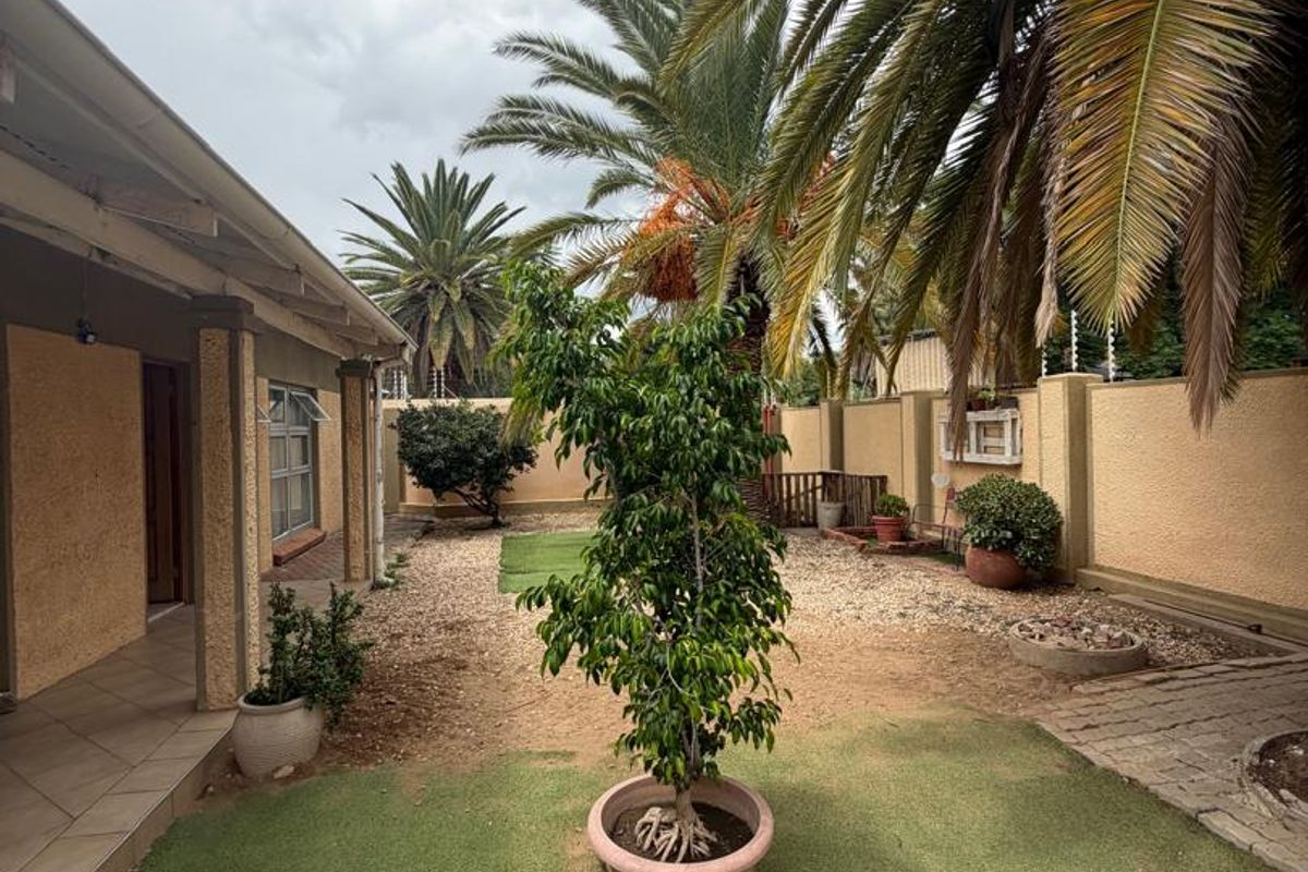 A rear garden area featuring a covered patio, paved sections, artificial lawn, and perimeter boundary walls with electric fencing.