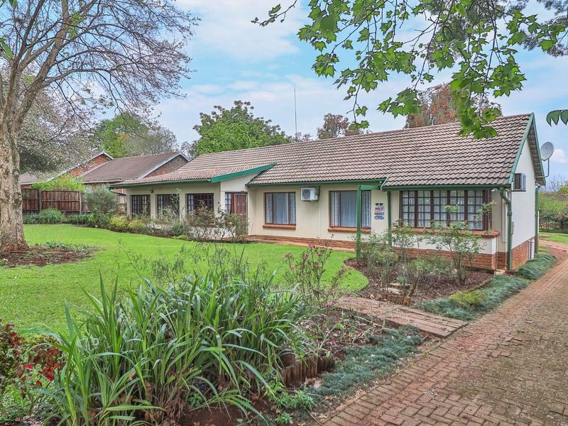 A view of the rear elevation of the house featuring a well-maintained garden, brick paved driveway, and tiled roof.