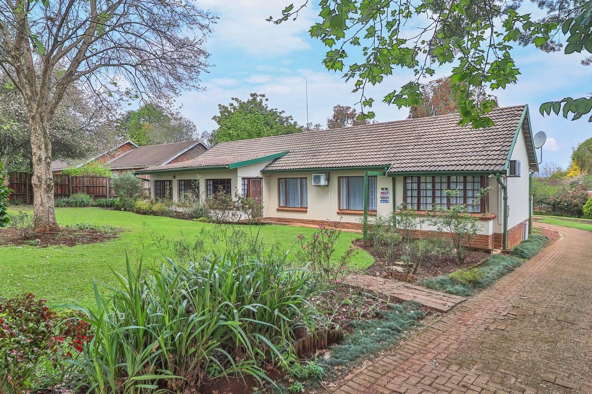 A view of the rear elevation of the house featuring a well-maintained garden, brick paved driveway, and tiled roof.