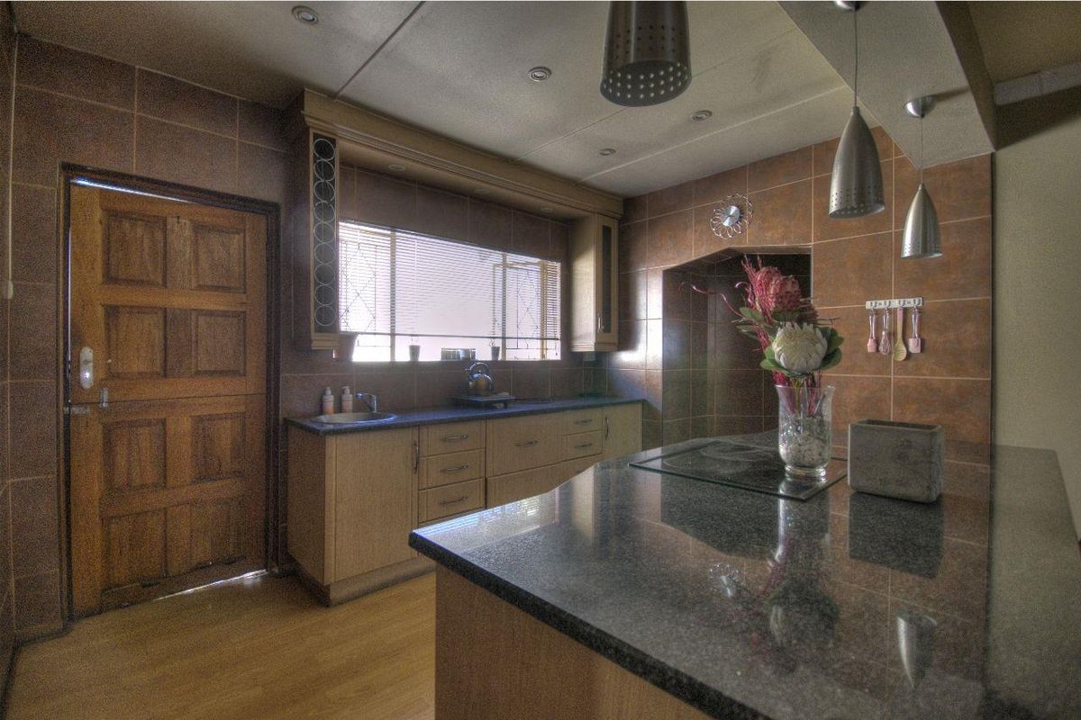 A functional kitchen featuring granite countertops, built-in cabinetry, and a central island with an integrated cooktop, finished with full-height wall tiling.