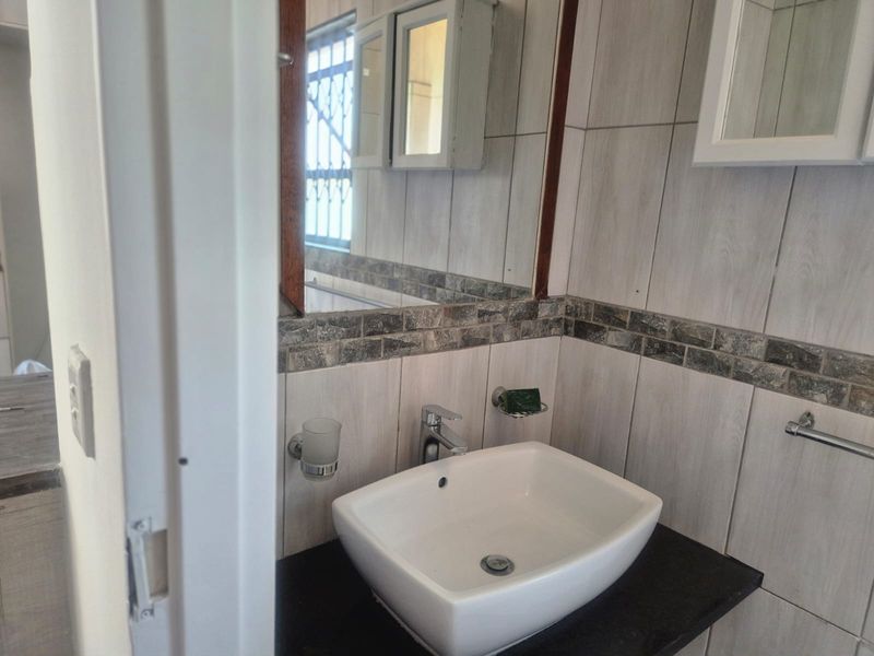 A functional bathroom featuring a modern vessel sink, dark vanity countertop, and tiled walls with a decorative border.