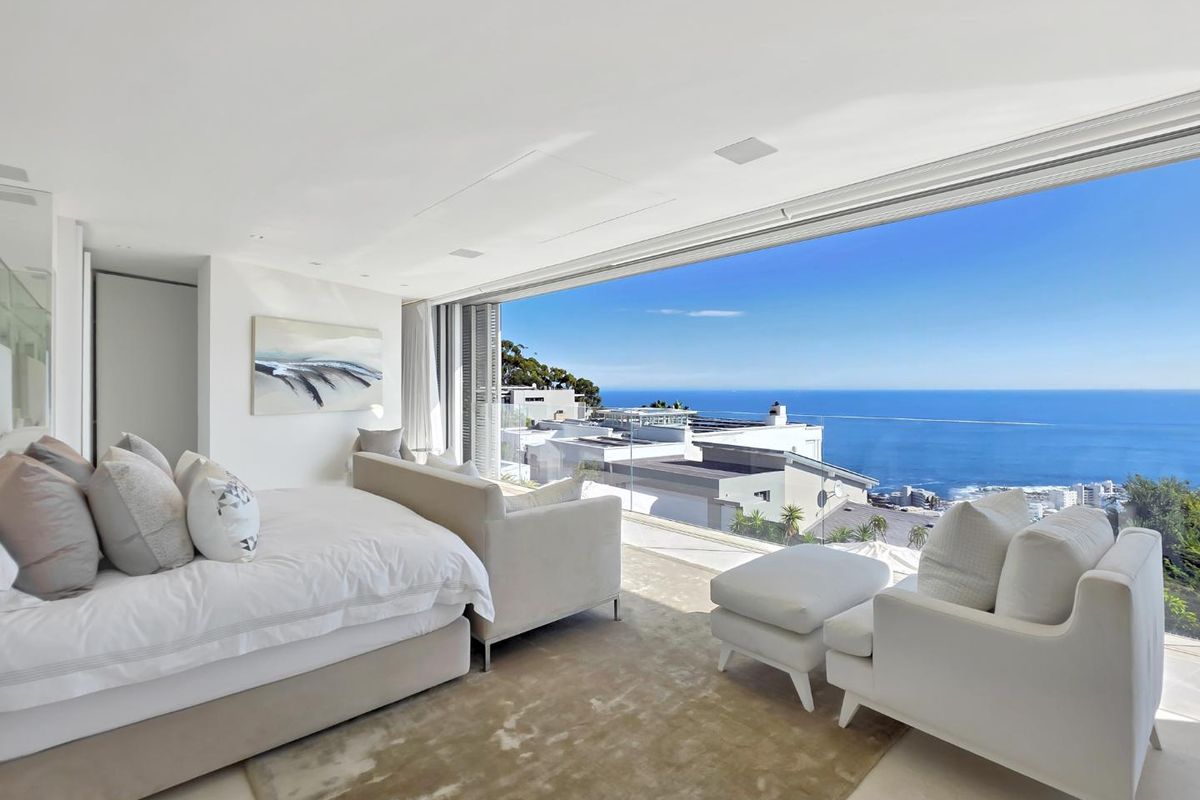 A luxurious bedroom featuring floor-to-ceiling glass sliding doors that open to a panoramic ocean view and a private balcony.