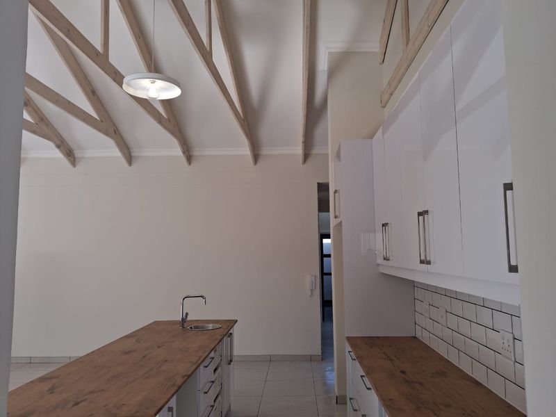Modern kitchen featuring a central island, white cabinetry, subway tile backsplash, and striking exposed timber rafters under a high vaulted ceiling.