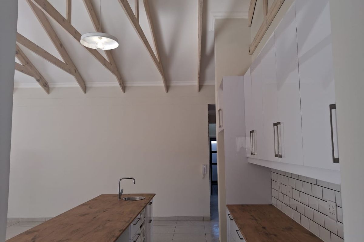 Modern kitchen featuring a central island, white cabinetry, subway tile backsplash, and striking exposed timber rafters under a high vaulted ceiling.