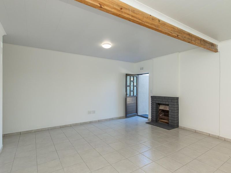 An empty living room featuring tiled flooring, a brick fireplace, and an exposed timber ceiling beam, with direct access to an outdoor area.