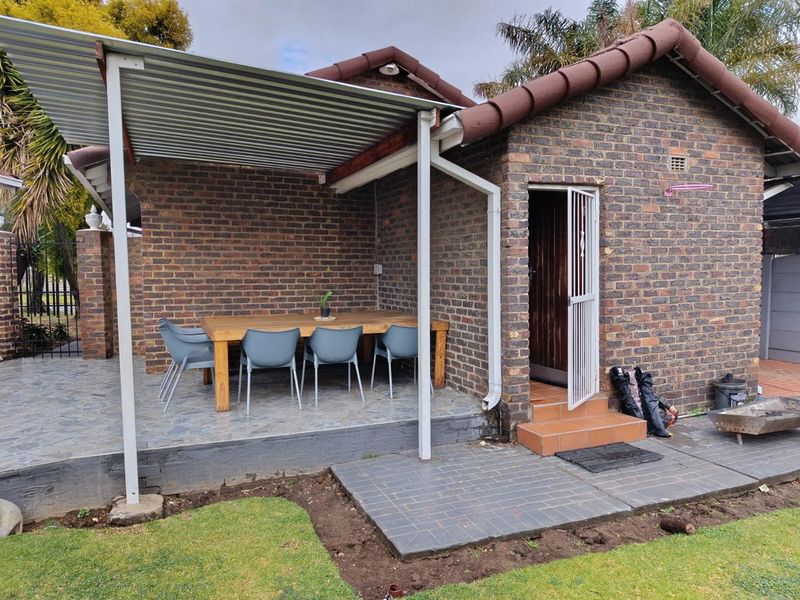 A covered outdoor patio area featuring brick construction, tiled flooring, and a corrugated metal roof, providing a functional space for outdoor dining.