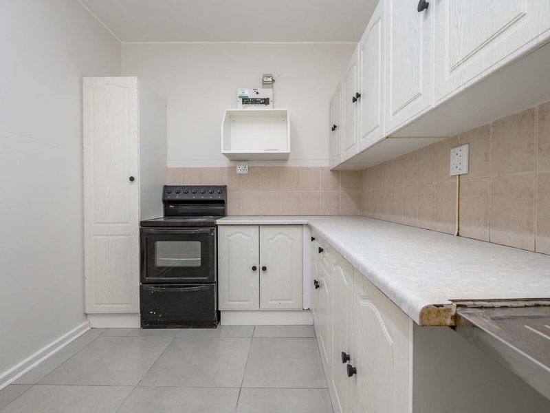 A functional kitchen featuring white cabinetry, tiled backsplash, laminate countertops, and a freestanding stove, offering a blank canvas for potential modern updates.