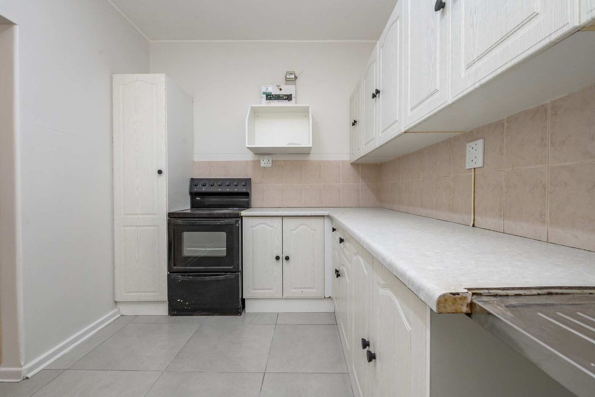 A functional kitchen featuring white cabinetry, tiled backsplash, laminate countertops, and a freestanding stove, offering a blank canvas for potential modern updates.
