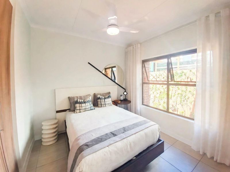 A bright and well-maintained bedroom featuring tiled flooring, a ceiling fan, and a large window allowing for natural light.