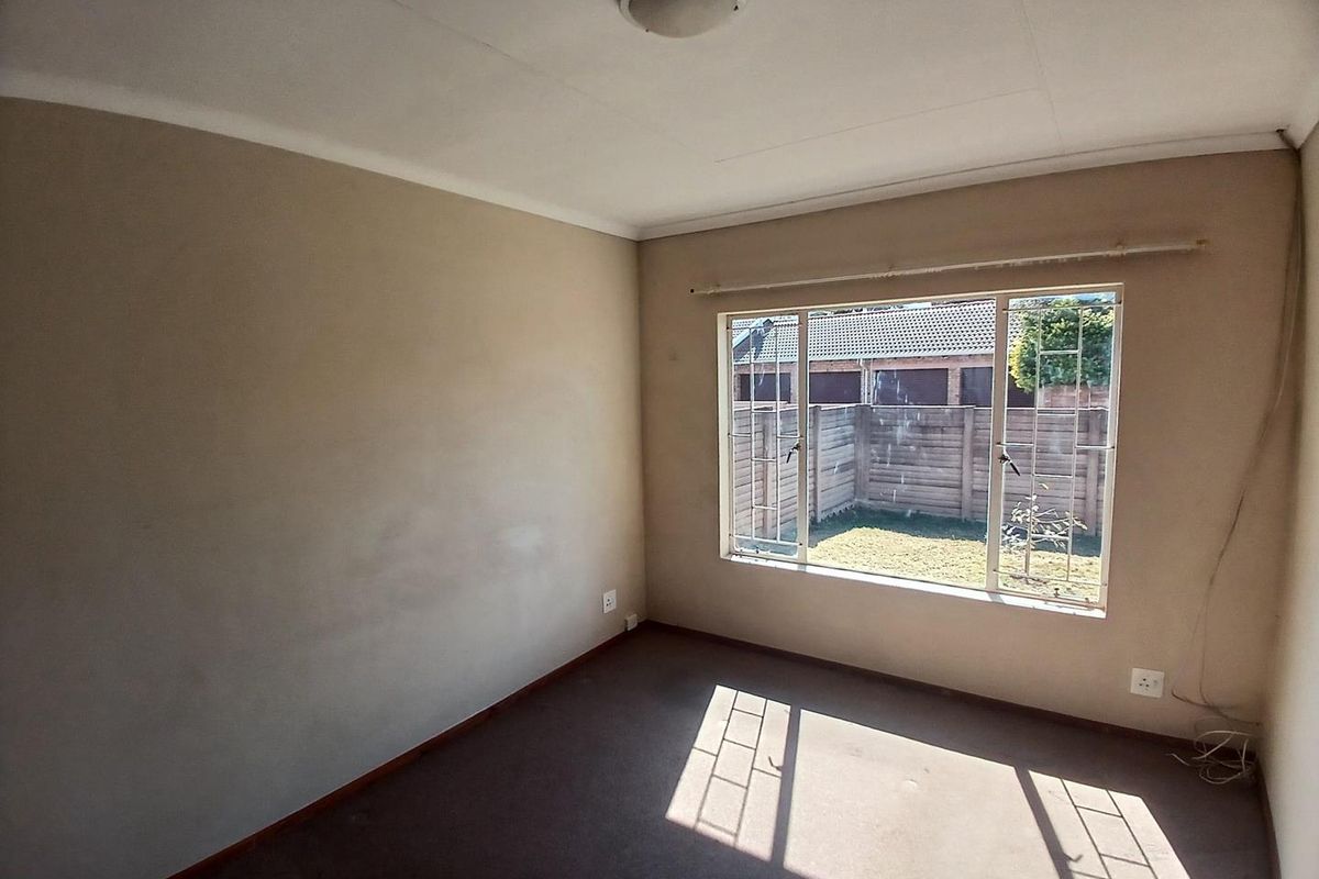An empty bedroom featuring carpet flooring, security bars on the window, and neutral wall tones, offering a blank canvas for personalization.