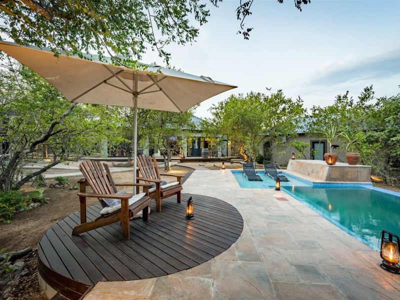 Outdoor pool area featuring a stone deck, a raised pool wall, and a circular wooden deck set within a landscaped garden environment.